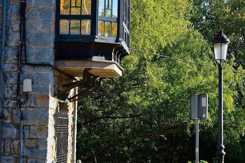 Un edificio de piedra con un balcón de madera, una farola y árboles verdes frondosos al fondo. 3