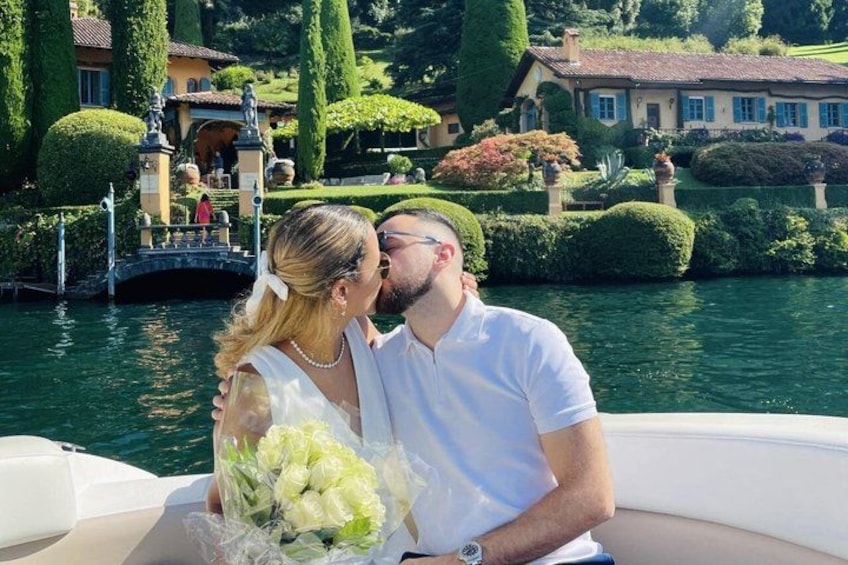 Un couple se trouve sur un bateau près d’un lac, avec un pont et des jardins bien entretenus en arrière-plan. 2