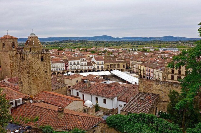 A historic town with a prominent tower, terracotta-roofed buildings, and a hilly landscape in the background. 5