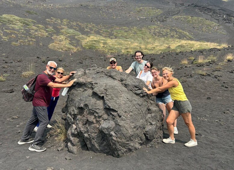A group of people interacting with a large volcanic rock formation. 2