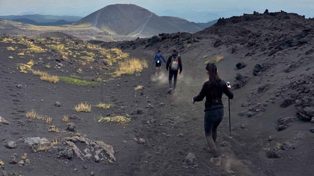 A group of hikers on a rocky trail with sparse vegetation, heading towards a mountainous landscape. 4