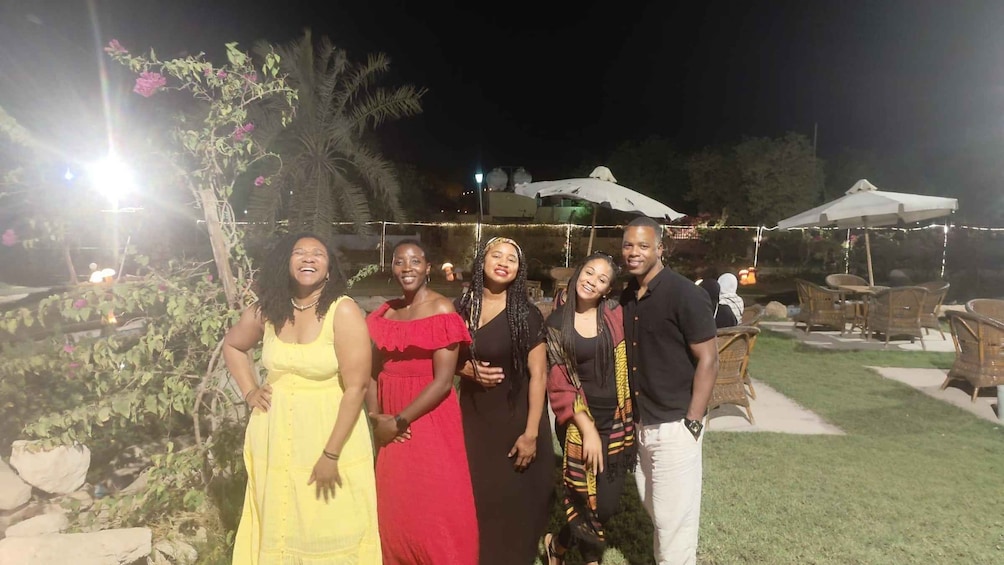 A group of people outdoors at night, standing in a garden with string lights and outdoor furniture. 2