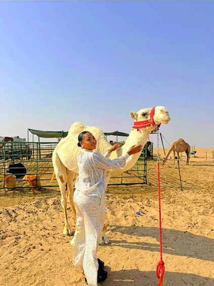 A person in a patterned outfit interacting with a camel in a desert enclosure. 1