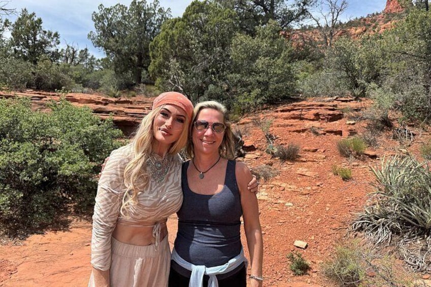 Two people standing in a desert landscape with red rock formations and sparse vegetation. 4