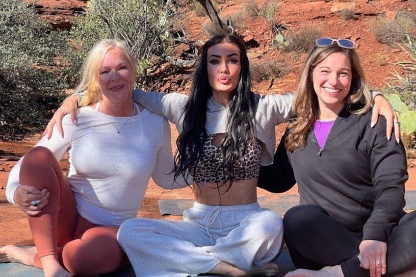 Three people sitting on the ground outdoors with red rock formations in the background. 3