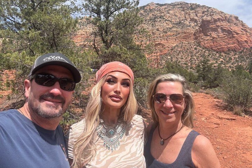 Three people in a desert landscape with red rock formations and sparse vegetation. 5