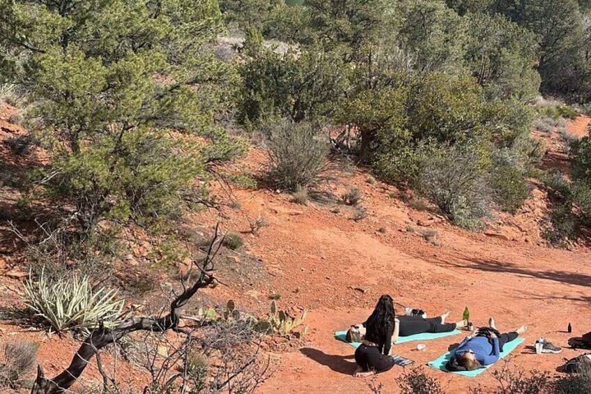 Two people meditating on a red dirt path surrounded by sparse vegetation. 4