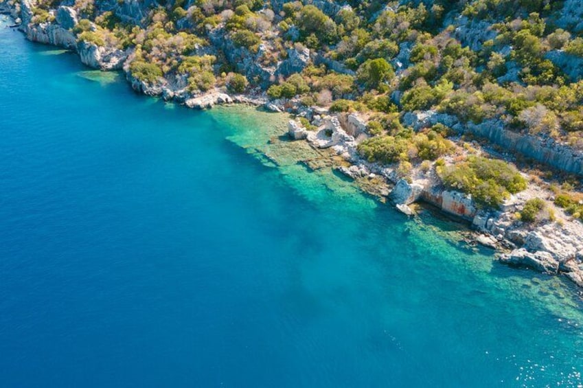 Een kustlandschap met helder turquoise water, rotsachtige kliffen en weelderige groene begroeiing. 2