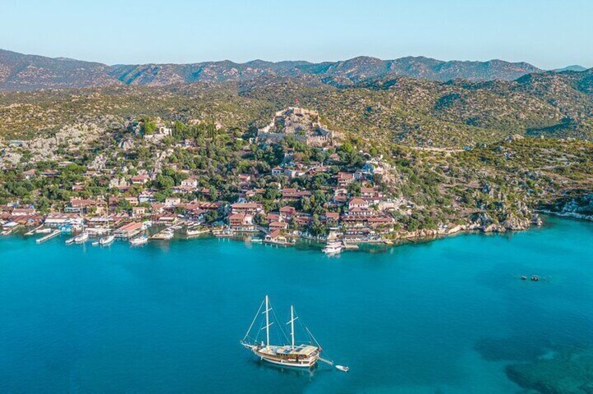 Vista aérea de un pueblo costero con una colina destacada, aguas azules cristalinas y varios barcos. 4