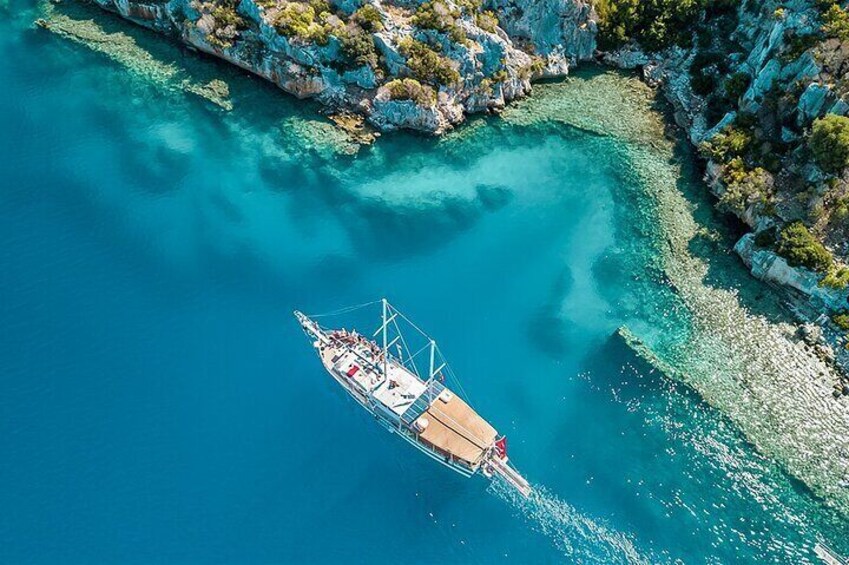 Vista aérea de un barco en aguas turquesas cristalinas cerca de acantilados rocosos. 3