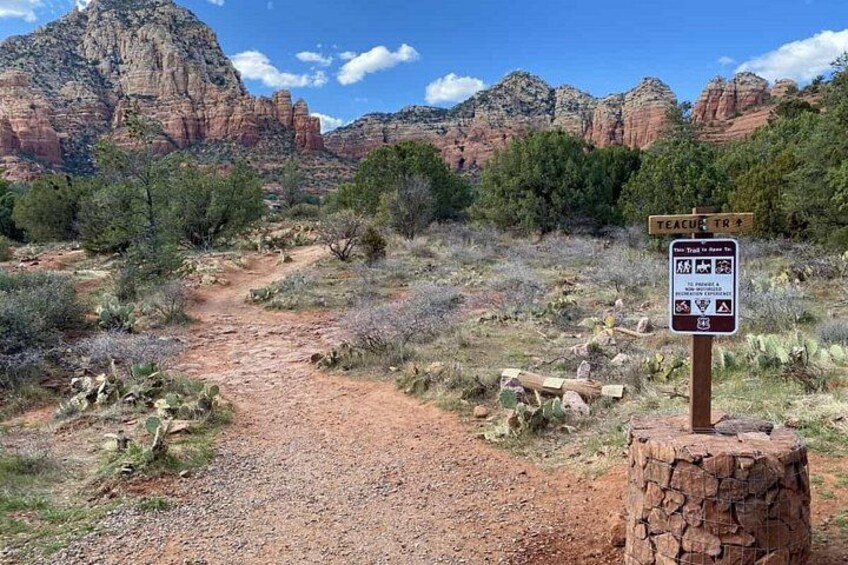 A dirt trail leading through a desert landscape with red rock formations in the background. 4