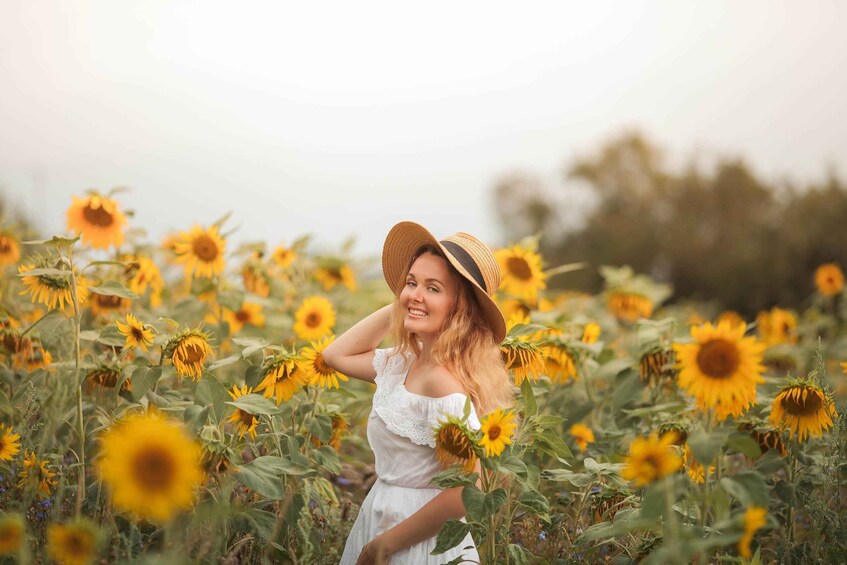 A person in a field of sunflowers wearing a straw hat and a white dress. 1