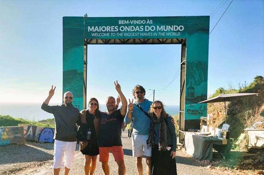 A group of people standing under a sign with a scenic view of the ocean. 1