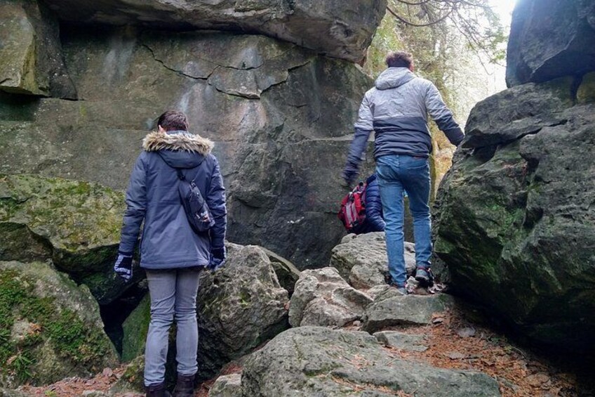 Two people hiking on a rocky trail surrounded by large boulders and trees. 1
