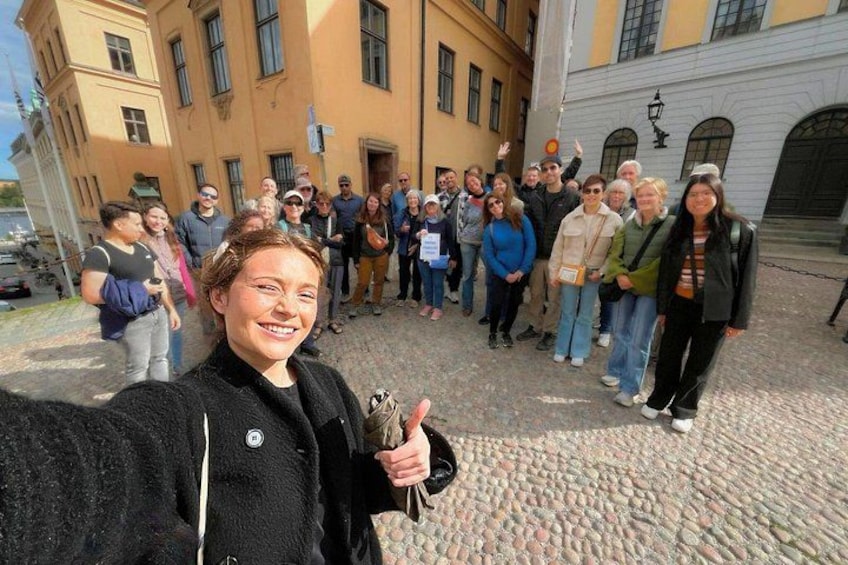 A group of people standing on a cobblestone street in front of a yellow building with arched windows. 5