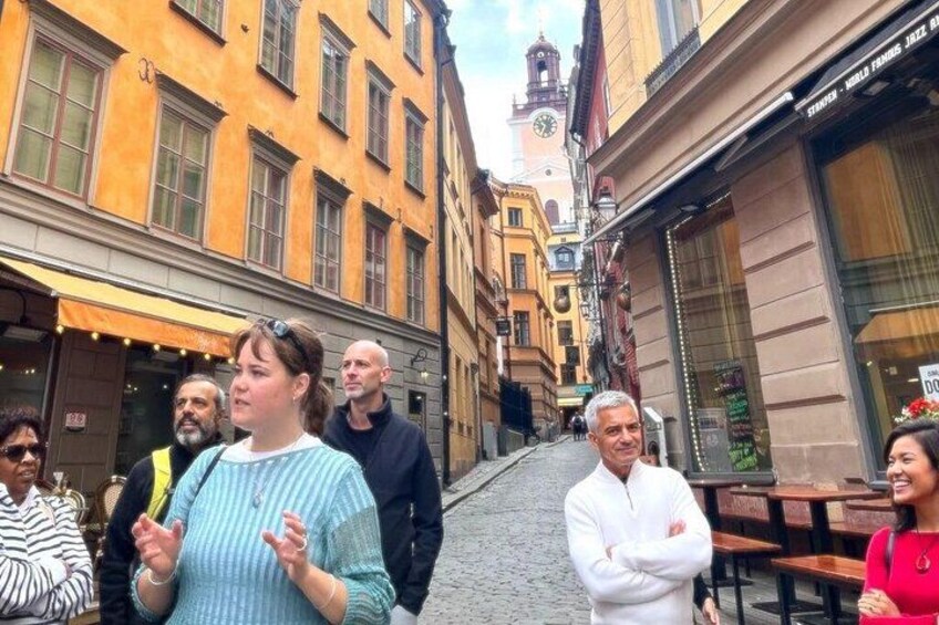 A cobblestone street lined with buildings, a clock tower, and outdoor seating areas. 4