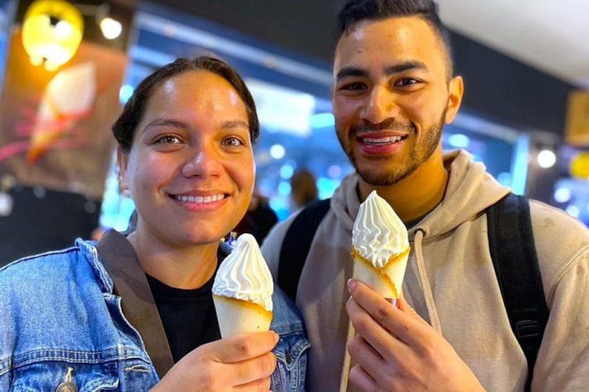 Two people holding ice cream cones in an indoor setting with bright lighting and a blurred background. 4