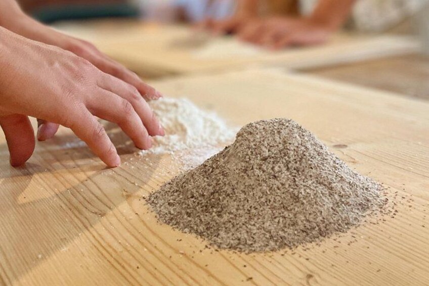 A person's hands mixing flour on a wooden surface. 3