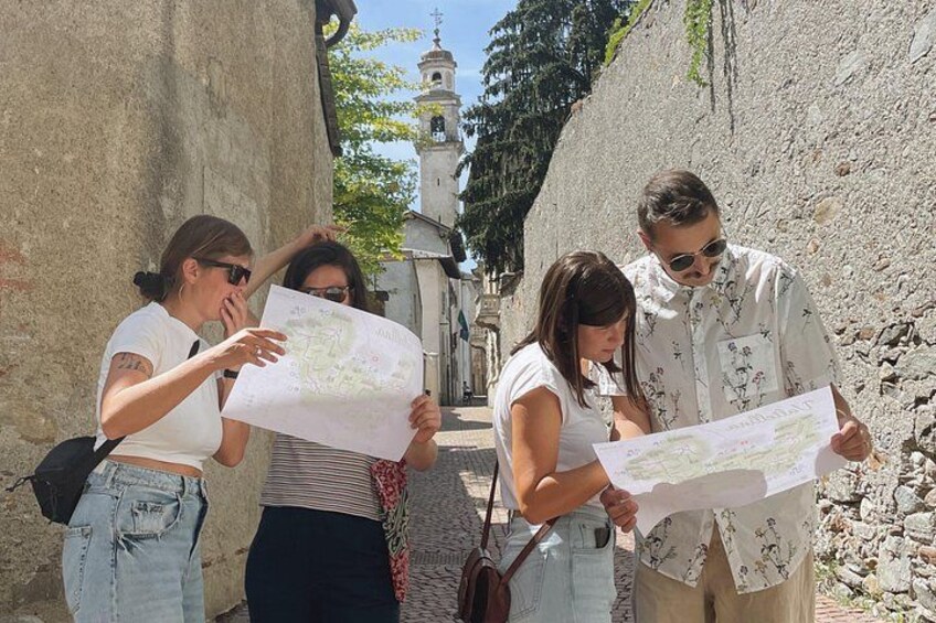 Four people examining a map in an outdoor setting with stone walls and a bell tower in the background. 2
