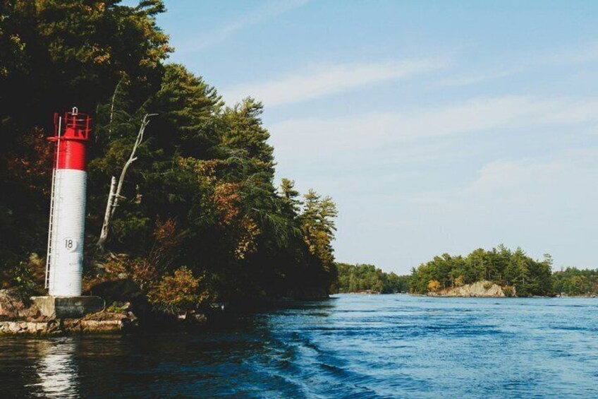 A lighthouse by a calm river, surrounded by dense trees. 4