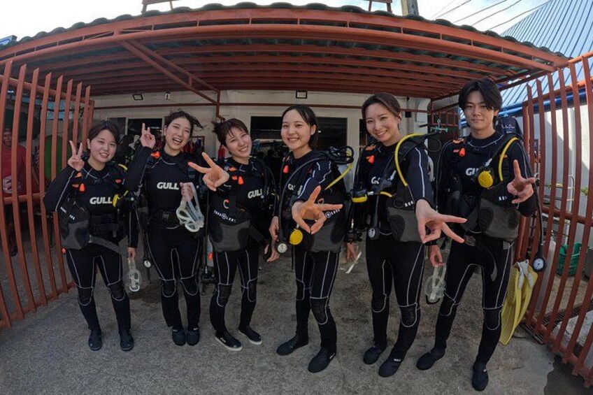 A group of people in scuba diving gear posing in front of a metal structure. 2