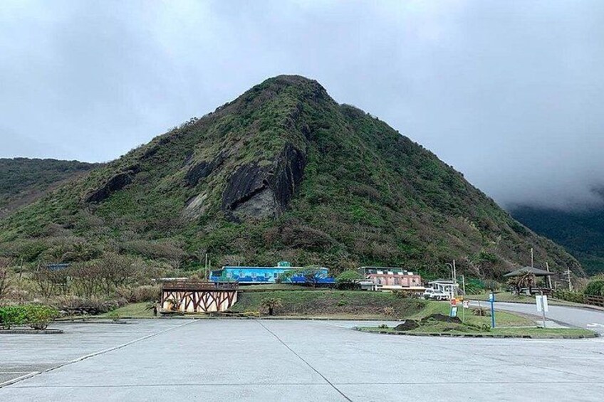 A mountain with a small settlement at its base, including a blue building and a bridge. 3