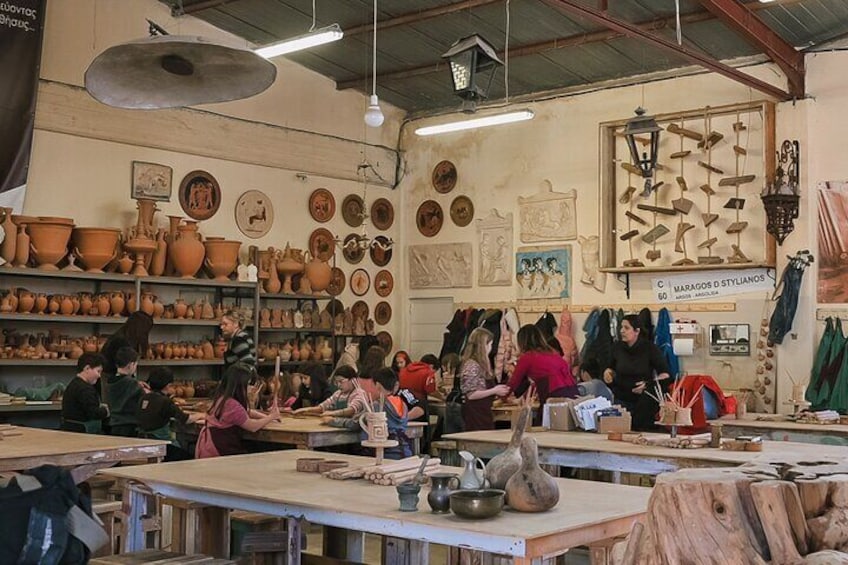 Un atelier de poterie avec des étagères remplies de poteries et des personnes travaillant à des tables. 1