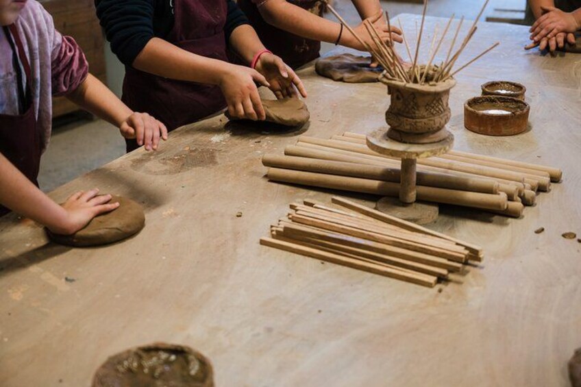 Kinderen die aan het pottenbakken zijn, met kleiballen en houten stokjes op een tafel. 2