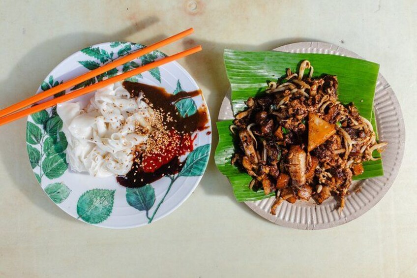 Two plates of food, one with noodles and the other with stir-fried meat, on a table with chopsticks. 3