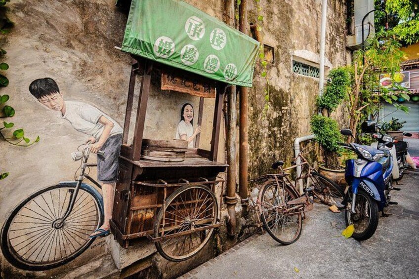 A street scene with a bicycle, a cart, and a scooter parked against a wall. 2