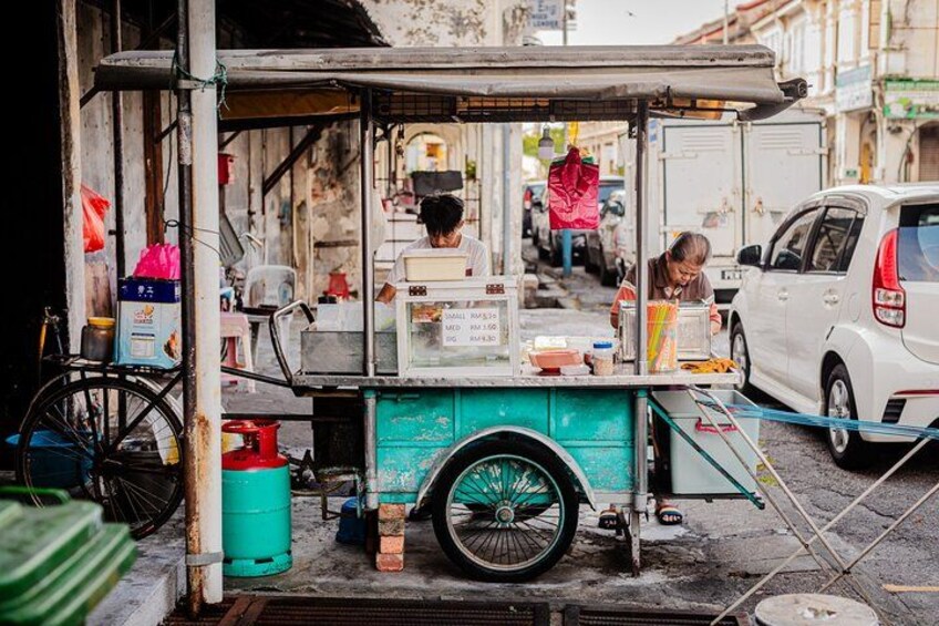 A street food cart with a person preparing food, a bicycle, and a white car parked nearby. 4