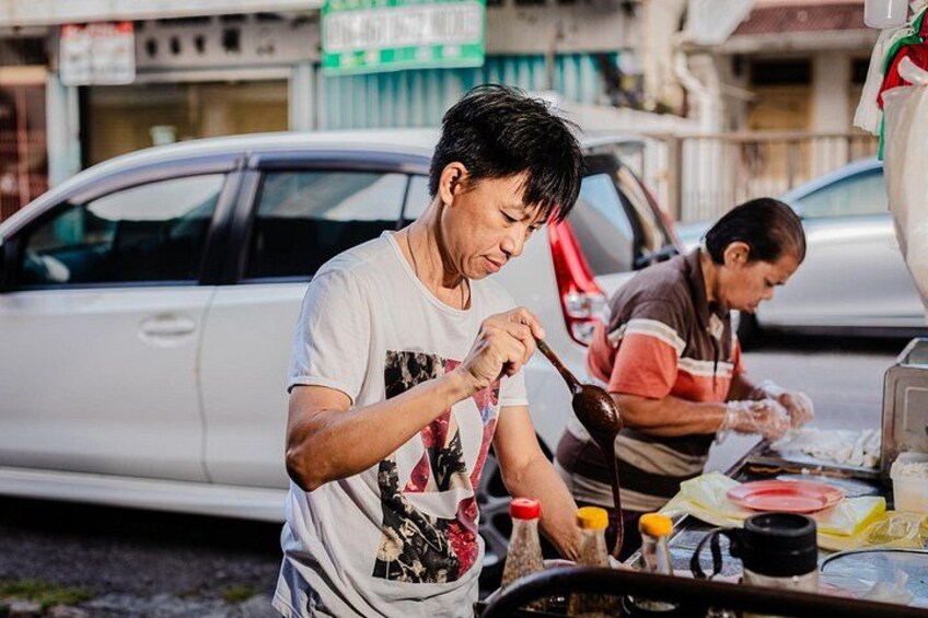 Two people cooking outdoors with a car and buildings in the background. 5