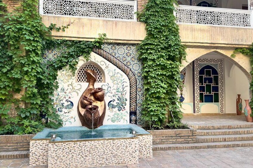 Una fuente con una escultura, rodeada de hiedra, frente a un edificio con detalles de azulejos intrincados y un balcón. 2