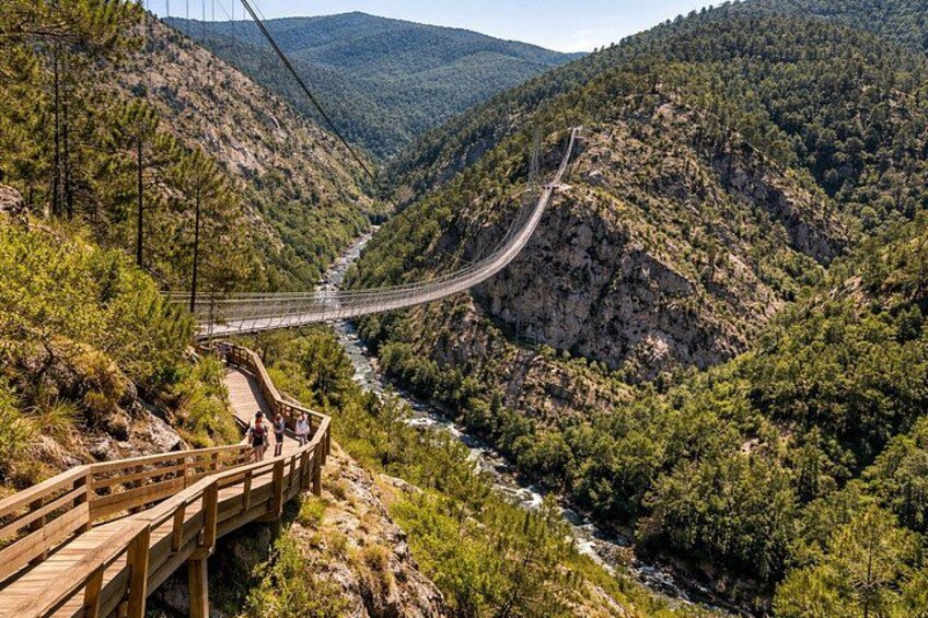 A wooden bridge over a river, surrounded by forested hills. 1