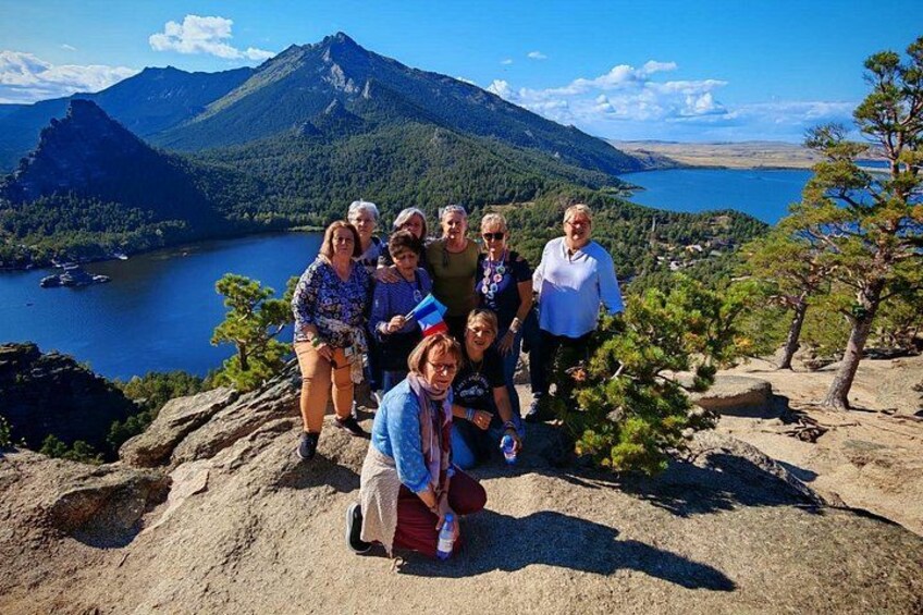Un grupo de personas sobre un promontorio rocoso, con una montaña y un lago al fondo. 5