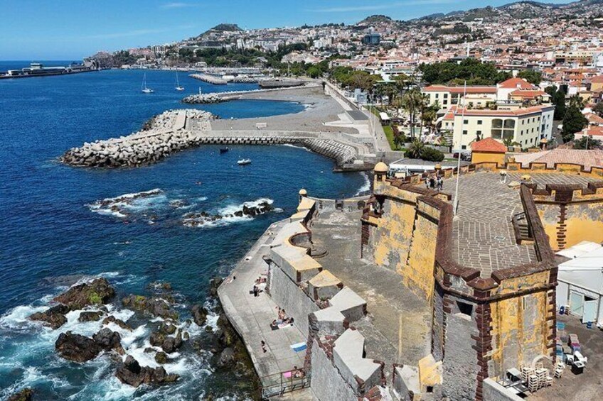 A coastal town with a fortified structure, a beach, and a rocky shoreline. 3