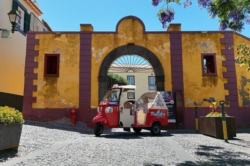 A vintage red ice cream truck parked in front of a yellow and red building with an arched entrance. 2