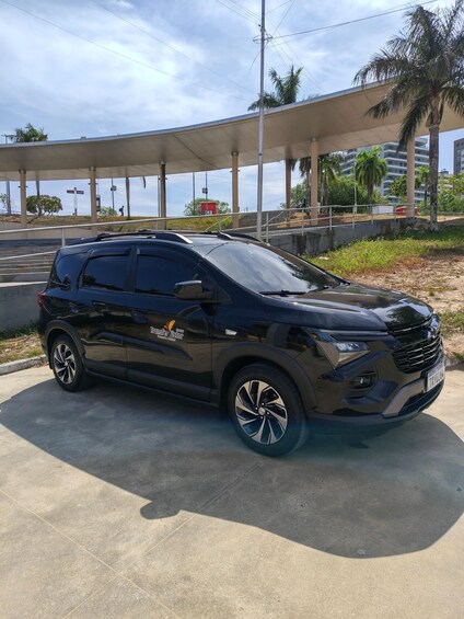 A black SUV parked under a covered area with palm trees and a building in the background. 2