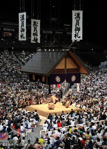 A sumo wrestling match in a large indoor arena with a crowd of spectators. 2