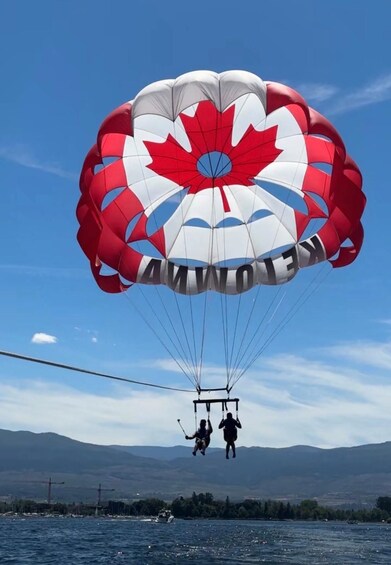 A person parasailing over a body of water with a parachute featuring a red maple leaf design. 2