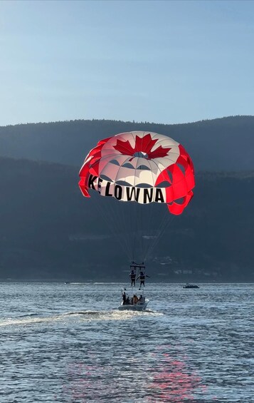 A parasailer with a red and white canopy over a body of water, with a forested hill in the background. 5