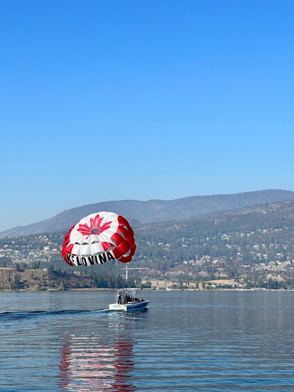 A parasailer with a red and white canopy over a body of water, a small boat, and a mountainous landscape in the background. 5