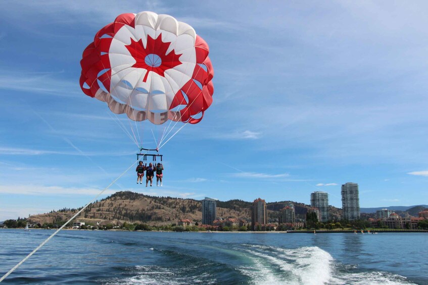 A parasailing activity with a red and white canopy over a group of people, a body of water, and a cityscape with buildings in the background. 4