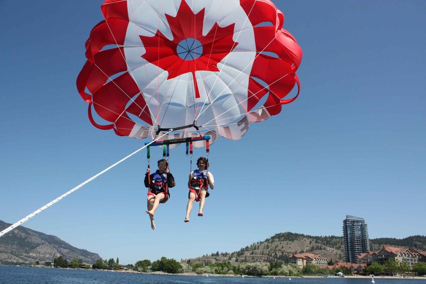 Two people parasailing over a body of water with a mountainous landscape in the background. 3