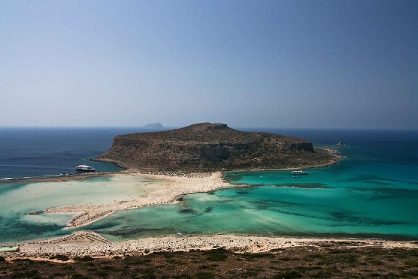 A coastal landscape with a prominent rocky island, clear turquoise waters, and a sandy beach. 2