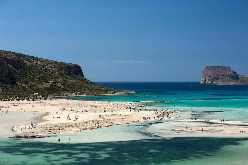 A beach with clear turquoise waters, a rocky cliff, and a distant island. 4