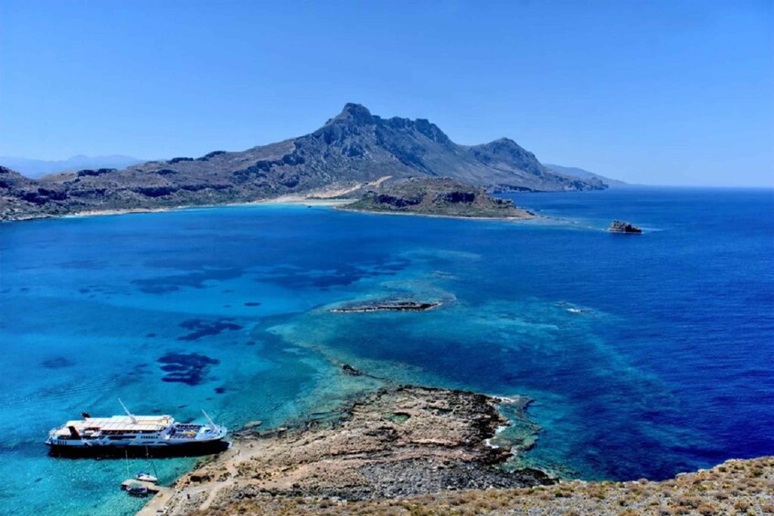 A coastal landscape with clear blue waters, a rocky shoreline, and a mountain in the background. 1