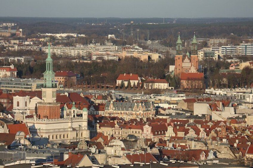 A cityscape with historic buildings, a prominent church with a green spire, and a large brick structure with a clock tower. 3