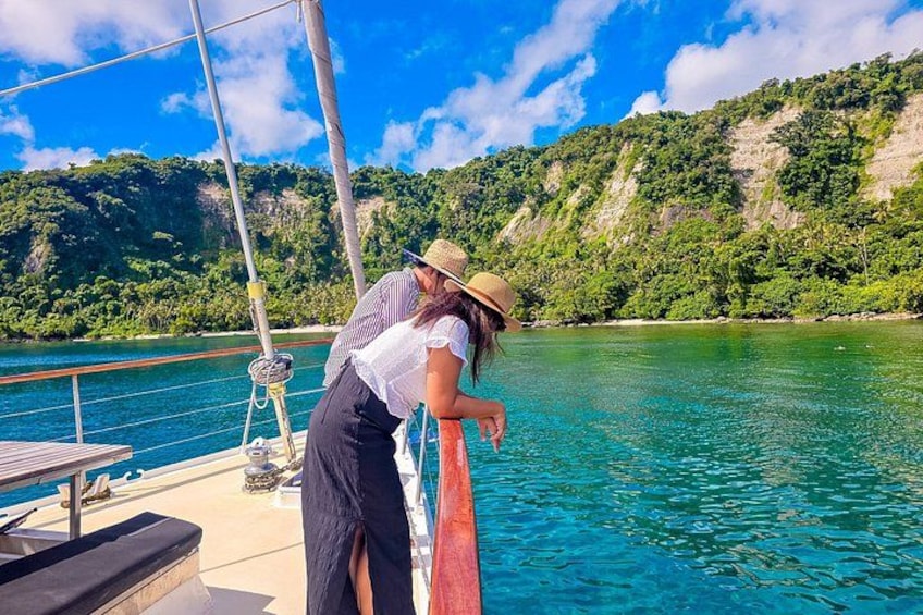 Un velero en un mar turquesa y transparente, con una isla boscosa al fondo. 1