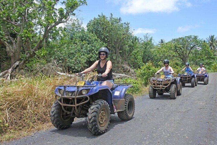 Three people riding ATVs on a rural road surrounded by vegetation. 2